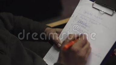 男人坐在椅子上，用蓝笔在文件夹里的纸单上划下划线